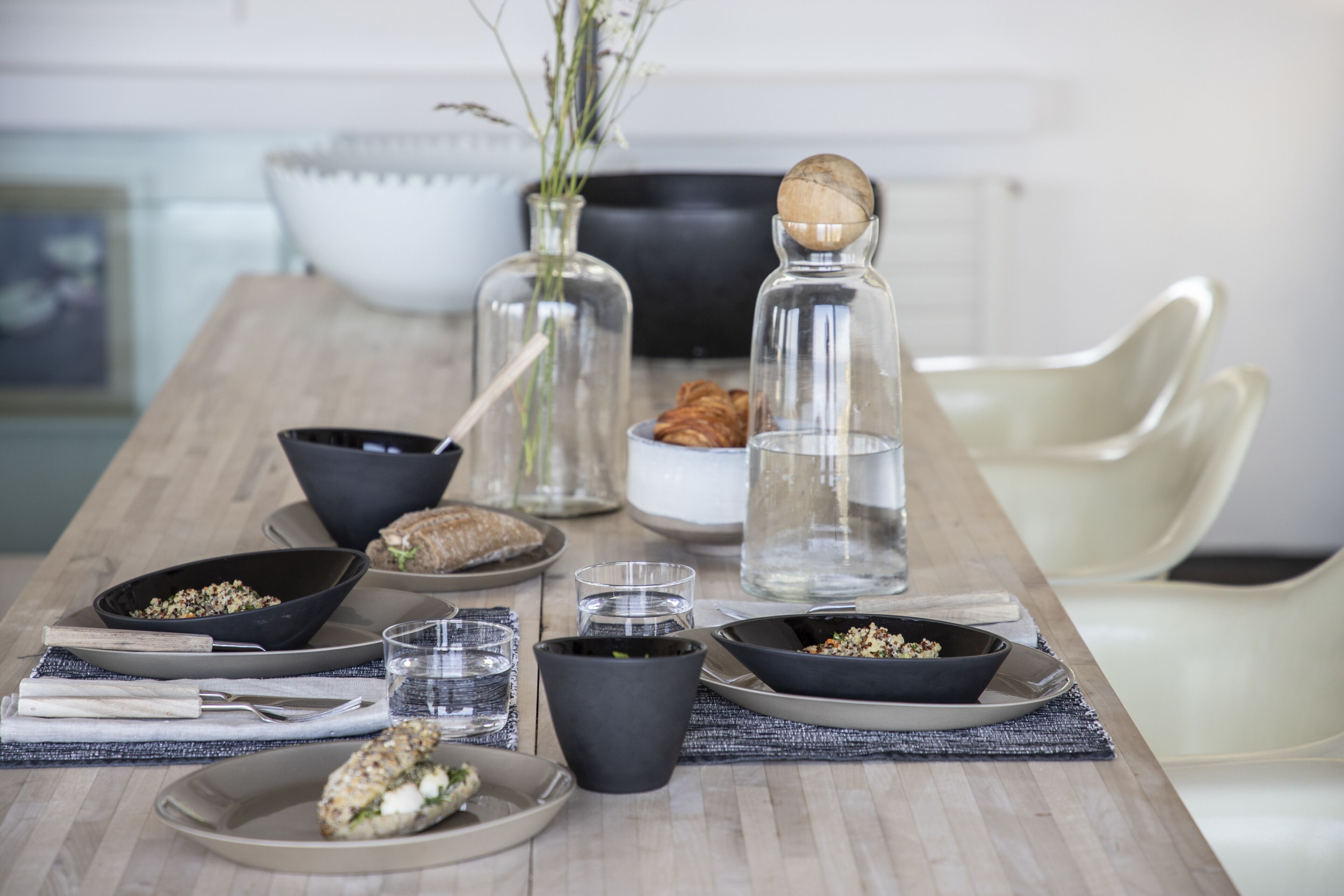Een eettafel gedekt met kommen, borden, glazen en een vaas met bloemen.