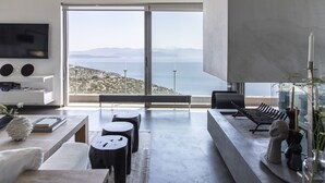 A modern living room with a large sliding glass door leading to a balcony with a view of the sea and mountains. - Sea View Villa Schinias (Marathon)