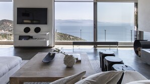A modern living room with a large TV, a coffee table with decorative items, and a view of the sea through large windows. - Sea View Villa Schinias (Marathon)