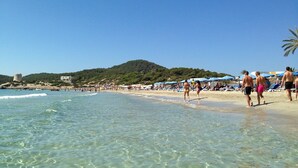 A beach with clear water, people walking, and umbrellas. - BEAUTIFUL VILLA IN THE HEART OF Playa den Bossa<br>ETV-2047-E (Playa den bossa, San jordi de ses Salines, IBIZA)