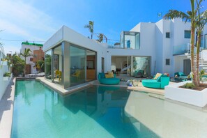 Uma área de piscina moderna com piscina envidraçada, mobiliário exterior azul-turquesa e uma escadaria que leva a um nível superior.