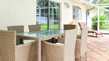 A patio area with wicker furniture, a glass-top table, and large windows.