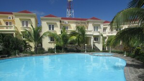 A swimming pool surrounded by buildings with balconies and a red-roofed tower in the background. - Golden Rod Villa, a fabulous establishment typical of the island mauritius! (flacq)