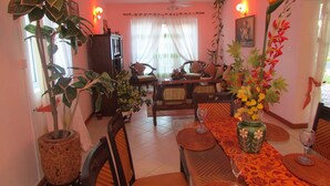 A dining area with a table set for two, surrounded by chairs, with a large potted plant and a vase of flowers on the table. - Golden Rod Villa, a fabulous establishment typical of the island mauritius! (flacq)