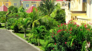 A row of yellow buildings with red roofs, surrounded by lush greenery and palm trees. - Golden Rod Villa, a fabulous establishment typical of the island mauritius! (flacq)