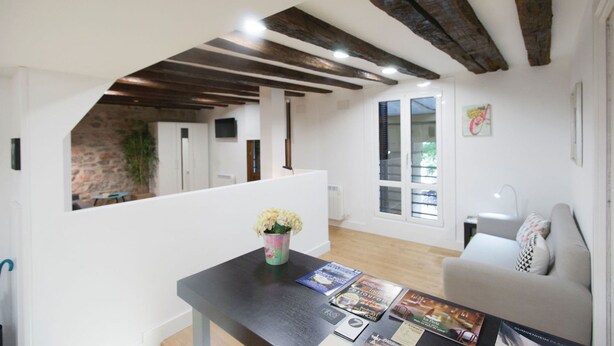 Un salon moderne avec un plafond en bois, un canapé blanc, une table basse avec des magazines et un vase de fleurs.