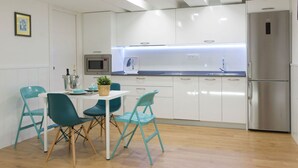 Une cuisine moderne avec des meubles blancs, un réfrigérateur en acier inoxydable et des chaises turquoise disposées autour d’une table blanche.