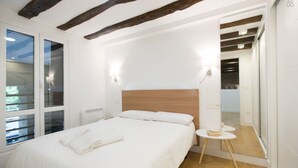 Une chambre avec un grand lit, des poutres en bois au plafond, une petite table ronde et un miroir au mur.