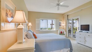 Un dormitorio con cama, televisor, ventilador de techo, ventana con contraventanas y vista al exterior.