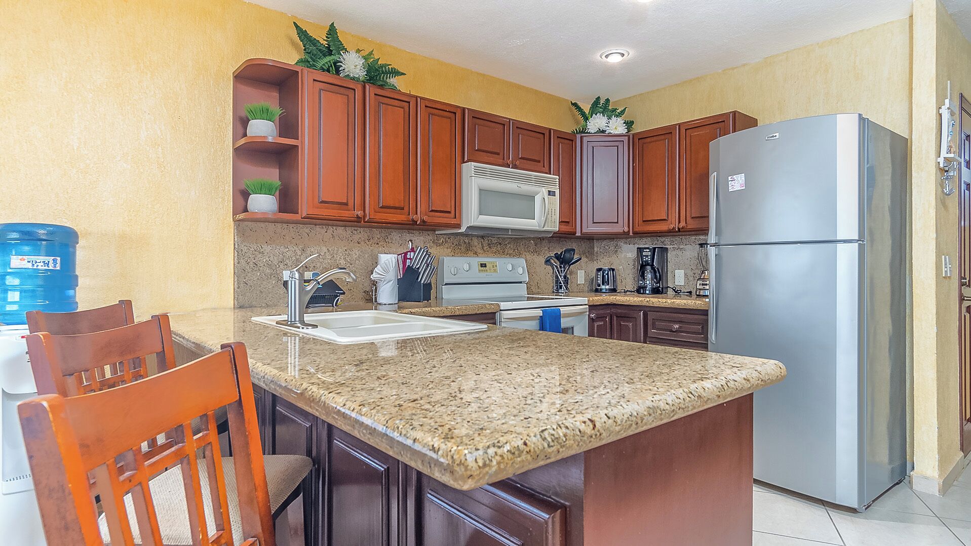 A kitchen with granite countertops, wooden cabinets, a stainless steel refrigerator, a microwave, and a stove.