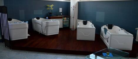 A modern bathroom with three white tubs, a glass coffee table, and a blue-tiled wall.