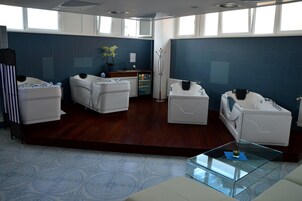 Uma casa de banho moderna com três banheiras brancas, uma mesa de centro de vidro e um revestimento de azulejos azuis.