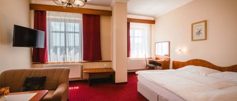 A hotel room with a bed, a desk, a chair, a television, and a window with curtains.