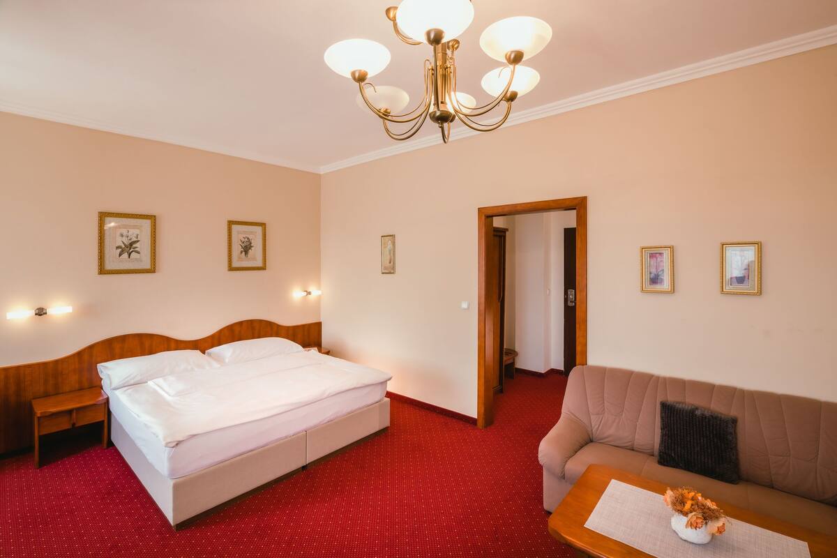 Una habitación de hotel con una cama, un sofá, una pequeña mesa con un jarrón y un candelabro.