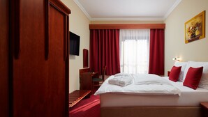 Een hotelkamer met een groot bed, rode gordijnen, een houten garderobe, een bureau en een televisie aan de muur.