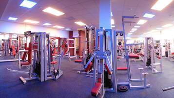 Un gimnasio con diferentes máquinas de ejercicio, un pilar azul y un banco rojo.