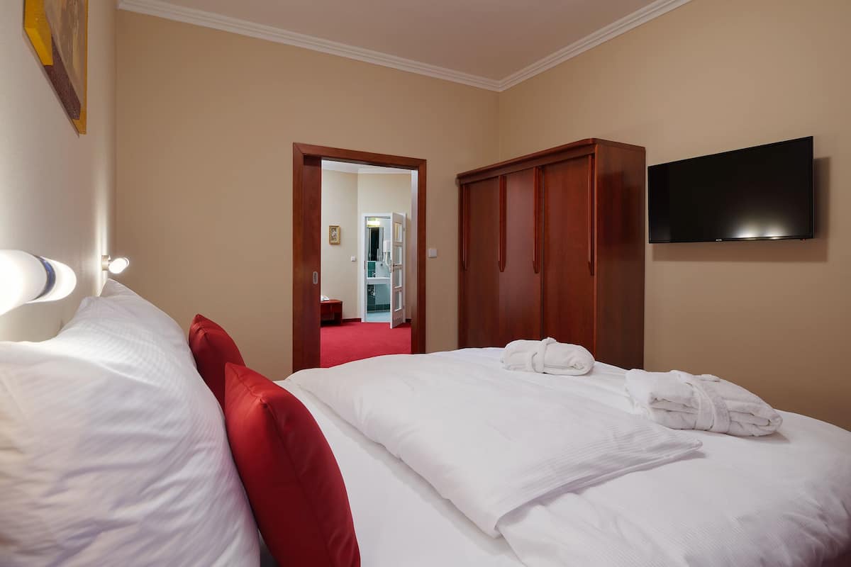 Habitación de hotel con cama, televisor, armario y baño visible a través de una puerta abierta.