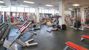 Een sportschool met diverse fitnessapparaten, banken en gewichten.