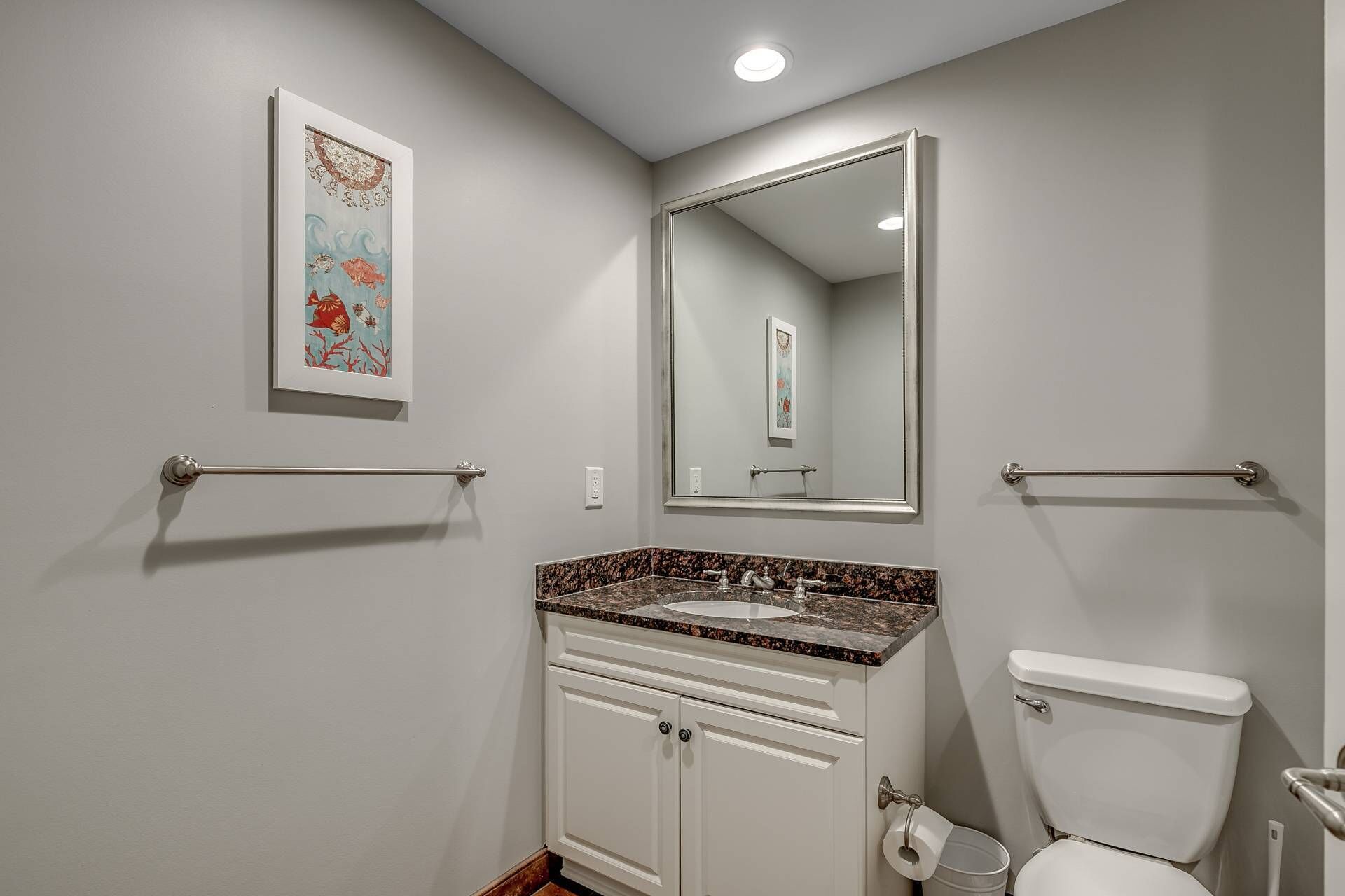 A bathroom with a white toilet, a sink with a granite countertop, a mirror above the sink, and a towel rack on the wall.