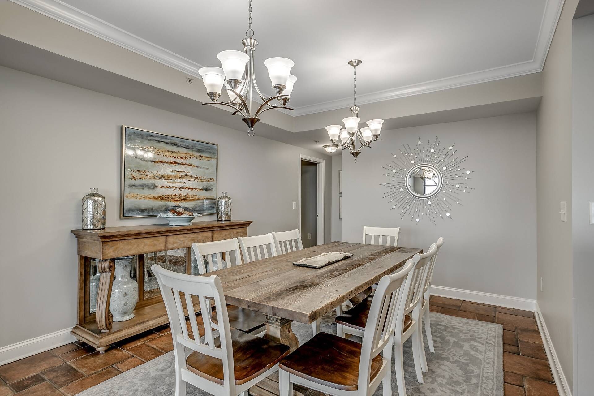 A dining room with a wooden table, white chairs, a chandelier, and a decorative mirror on the wall.