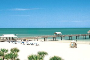 A beach with a pier, beach umbrellas, and a lifeguard tower. - Sandcastle U3261 - Little Harbor Beach Resort - Tampa Bay (Ruskin)