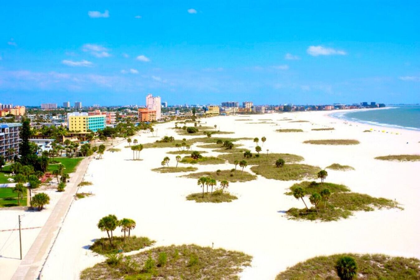 A beach with white sand, palm trees, and a cityscape in the background.