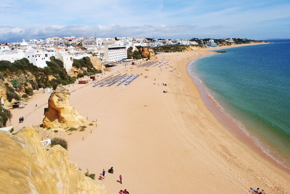A coastal beach with a sandy shore, a few umbrellas, and buildings in the background.