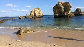 A beach with clear water, rocky formations, and a sandy shore.