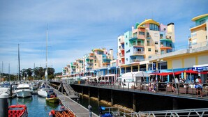 Een jachthaven met kleurrijke gebouwen, boten en een steiger met mensen.
