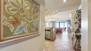 A spacious kitchen with a central island, a dining area with a glass table, and a large decorative painting on the wall. - 303W - Stay at the beach in this Elegant 2BR Condo! (Orange Beach)