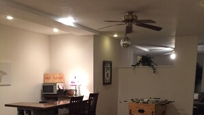 Una sala de estar con comedor, ventilador de techo, televisor y mesa de fútbol.