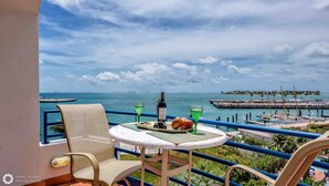 Un balcon avec une table dressée pour deux personnes, donnant sur une marina et la mer.