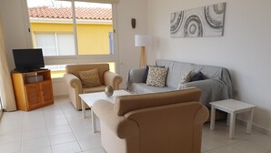 Ein Wohnzimmer mit einer Couch, zwei Sesseln, einem Couchtisch und einer TV-Konsole.