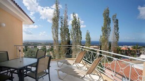 Ein Balkon mit Tisch und Stühlen mit Blick auf die Küste, Bäume und Gebäude.