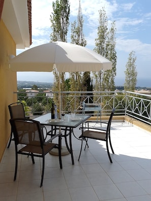 A terrace with a table and chairs, a white umbrella, and a view of the landscape. - Penthouse Sea View Apartment in Tala, Paphos, Cyprus in quiet location with pool (Tala)