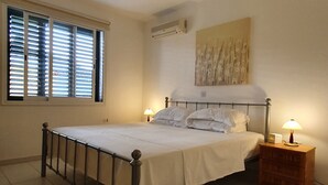 Ein Schlafzimmer mit Bett, Nachttischen, Deckenventilator und Fenster mit Jalousien.