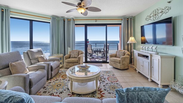 A spacious living room with a large window offering a view of the ocean, a ceiling fan, and a flat-screen TV. - SeaChase 503W RARE Reserved Covered Parking Included FREE (Orange Beach)