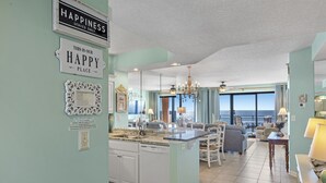 A spacious kitchen with a central island, a dining area with a view, and a living room with a chandelier. - SeaChase 503W RARE Reserved Covered Parking Included FREE (Orange Beach)