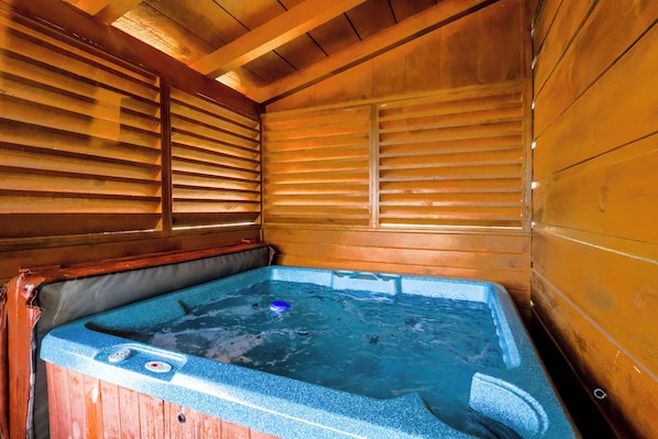 A wooden cabin with a hot tub, wooden walls, and a sloped ceiling.