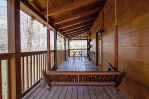 A wooden porch with a swing, a table, and chairs.