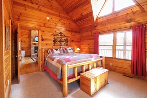 A wooden cabin bedroom with a bed, a bench, a window with curtains, and a fireplace.
