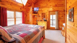 A wooden cabin bedroom with a bed, a television, a dresser, and a window with curtains. - One of the coziest log cabins in the Smokies! With a hot tub and a jacuzzi tub! (Pigeon Forge)