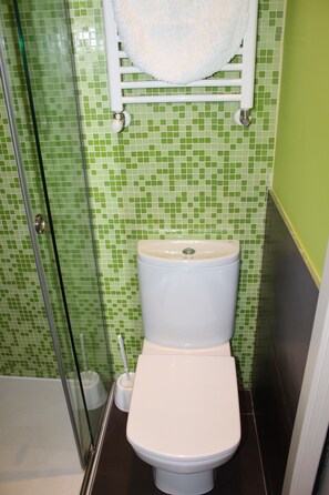 A bathroom with a toilet, a glass shower enclosure, and a green mosaic tile wall.
