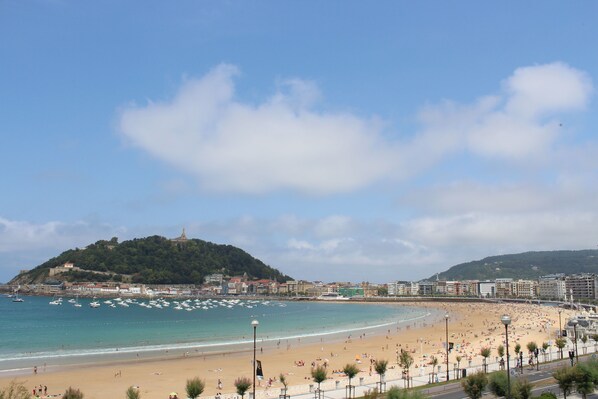 A beach with a hill in the background, a promenade, and a clear sky.