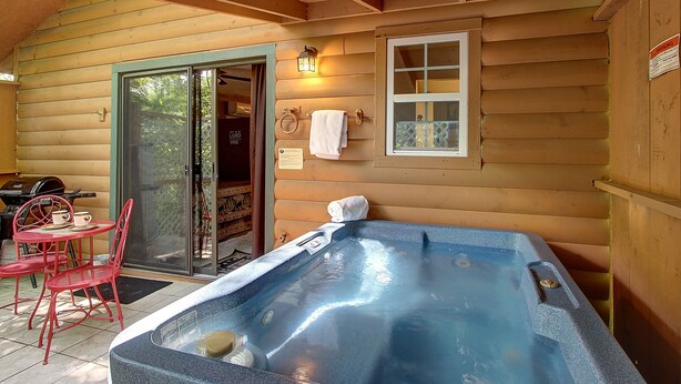 A wooden cabin with a hot tub, red chairs, and a glass door leading to a room. - Cozy 1BR with log cabin near Pigeon Forge Parkway (Pigeon Forge)