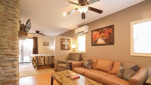 A living room with a sofa, a coffee table, a television on a stand, a ceiling fan, and a window with a view. - Cozy 1BR with log cabin near Pigeon Forge Parkway (Pigeon Forge)