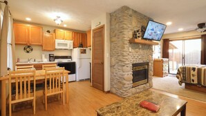 A kitchen with wooden cabinets, a stone fireplace, a television mounted on the wall, and a dining area with a table and chairs. - Cozy 1BR with log cabin near Pigeon Forge Parkway (Pigeon Forge)