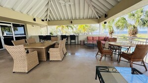 A covered outdoor patio with wicker furniture, a glass table, and a view of the ocean.