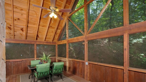 A wooden-paneled room with a ceiling fan, large windows, a table with chairs, and a potted plant. - Cutest, comfiest log cabin with great screened in porch! (Sevierville)
