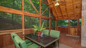 A wooden deck with a glass table and chairs, surrounded by a forest. - Cutest, comfiest log cabin with great screened in porch! (Sevierville)